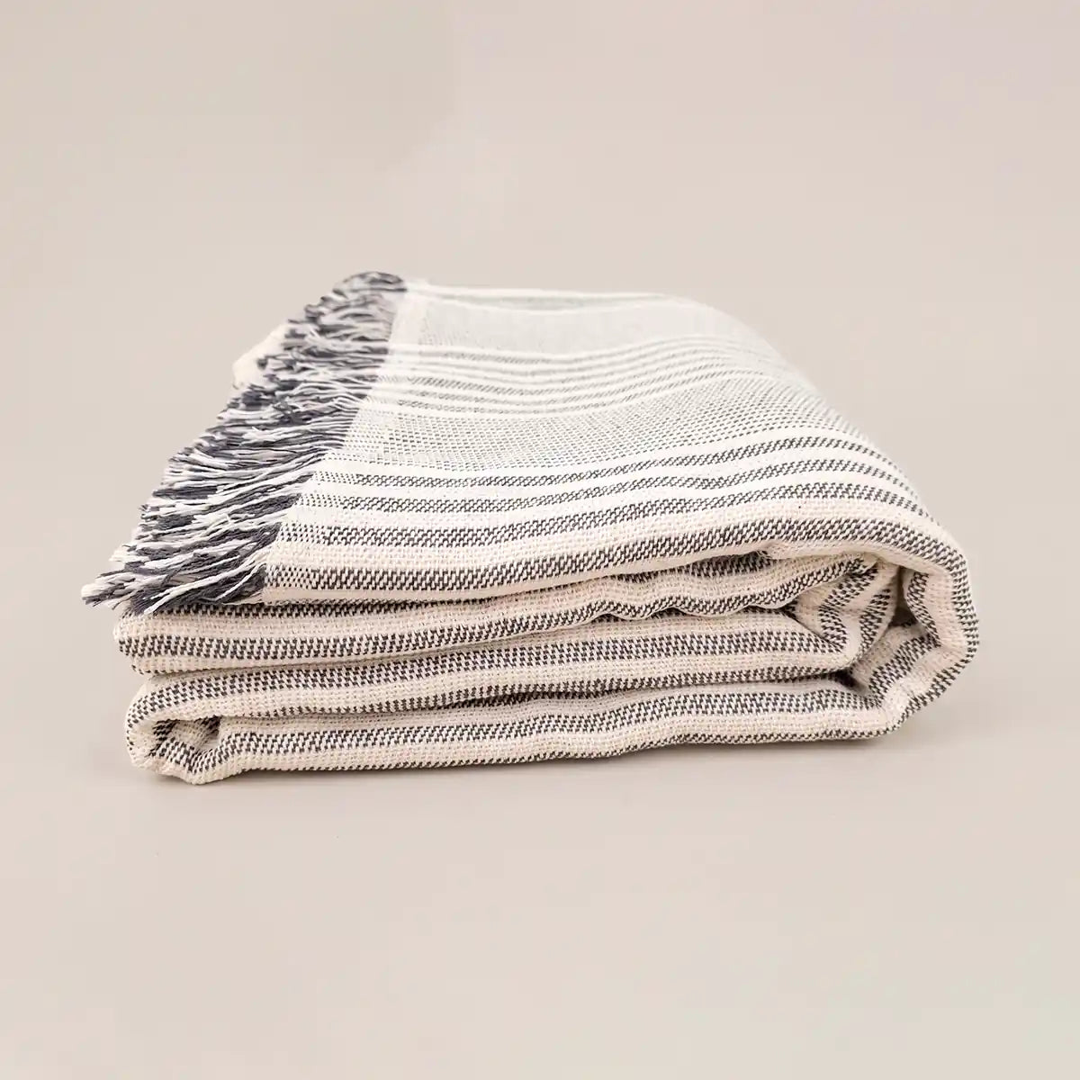 Colcha de algodón a rayas grises doblada y apilada, destacando el grosor ideal para el verano y la textura suave del hilo sostenible.