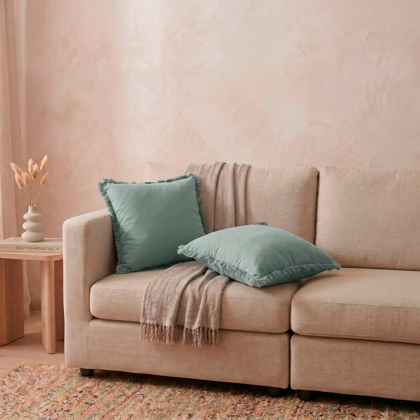 Combinación relajante de cojines decorativos en el sofá, destacando la delicada funda azul claro de algodón natural con flecos de Oma Home.