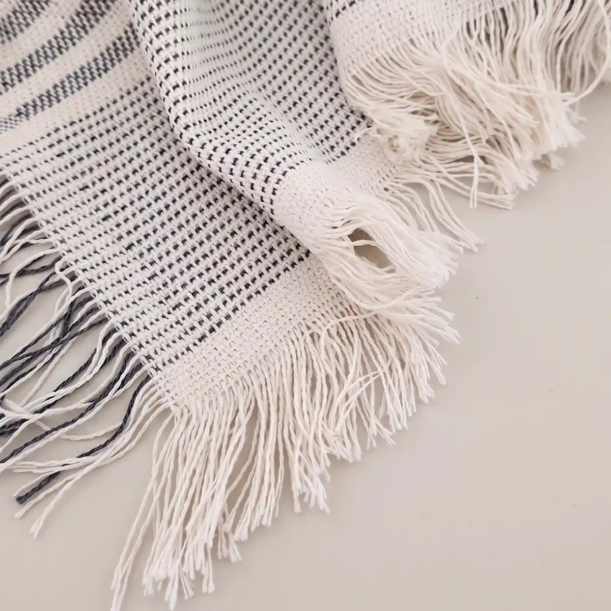 Detalle de los flecos decorativos en tonos gris y crudo de la colcha de verano, mostrando la alta calidad del acabado textil.