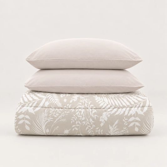 Piumone invernale beige con stampa di foglie bianche, piegato ordinatamente con due federe abbinate.