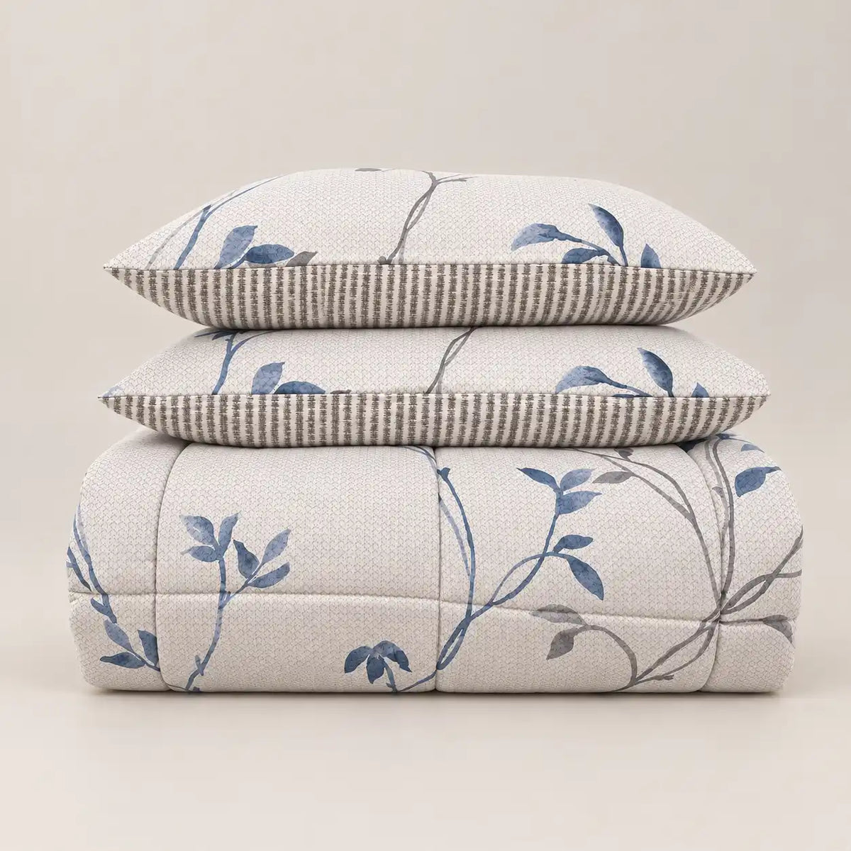 Piumone invernale con stampa floreale blu e retro a righe, piegato ordinatamente con due federe abbinate.