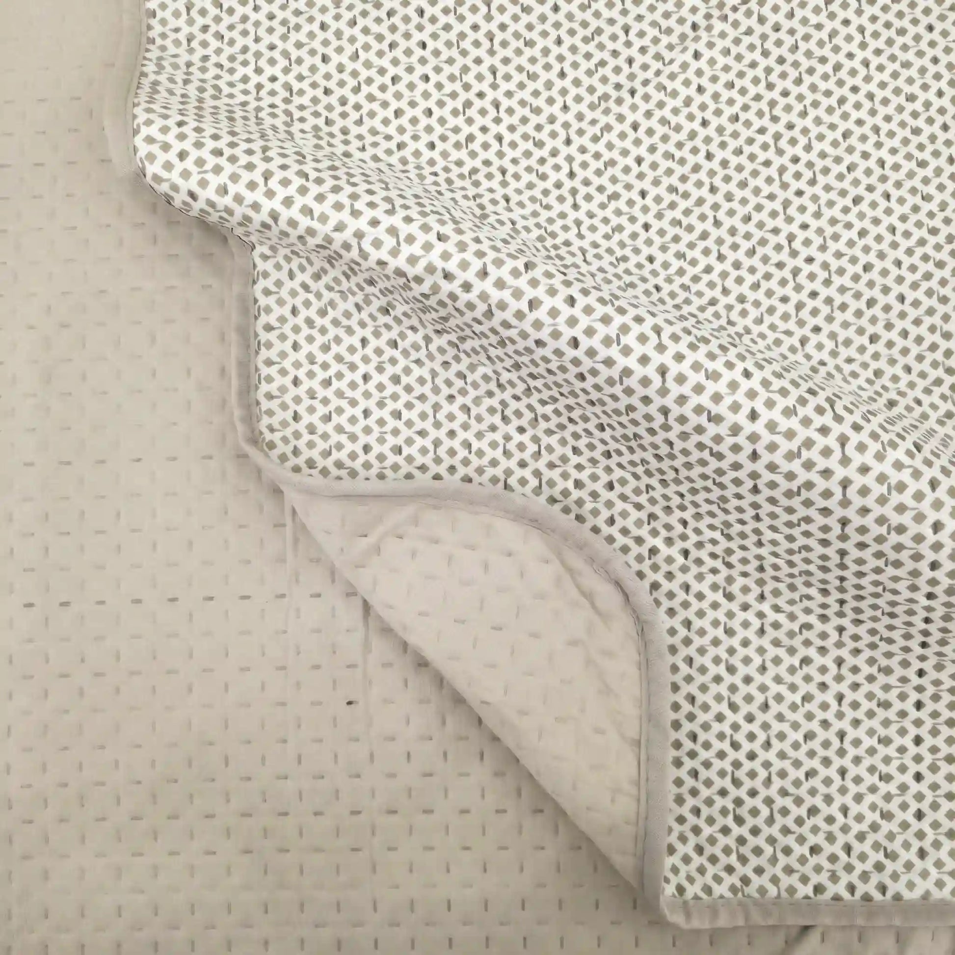 Detalle de las esquinas redondeadas y caída de la colcha de verano beige en la cama