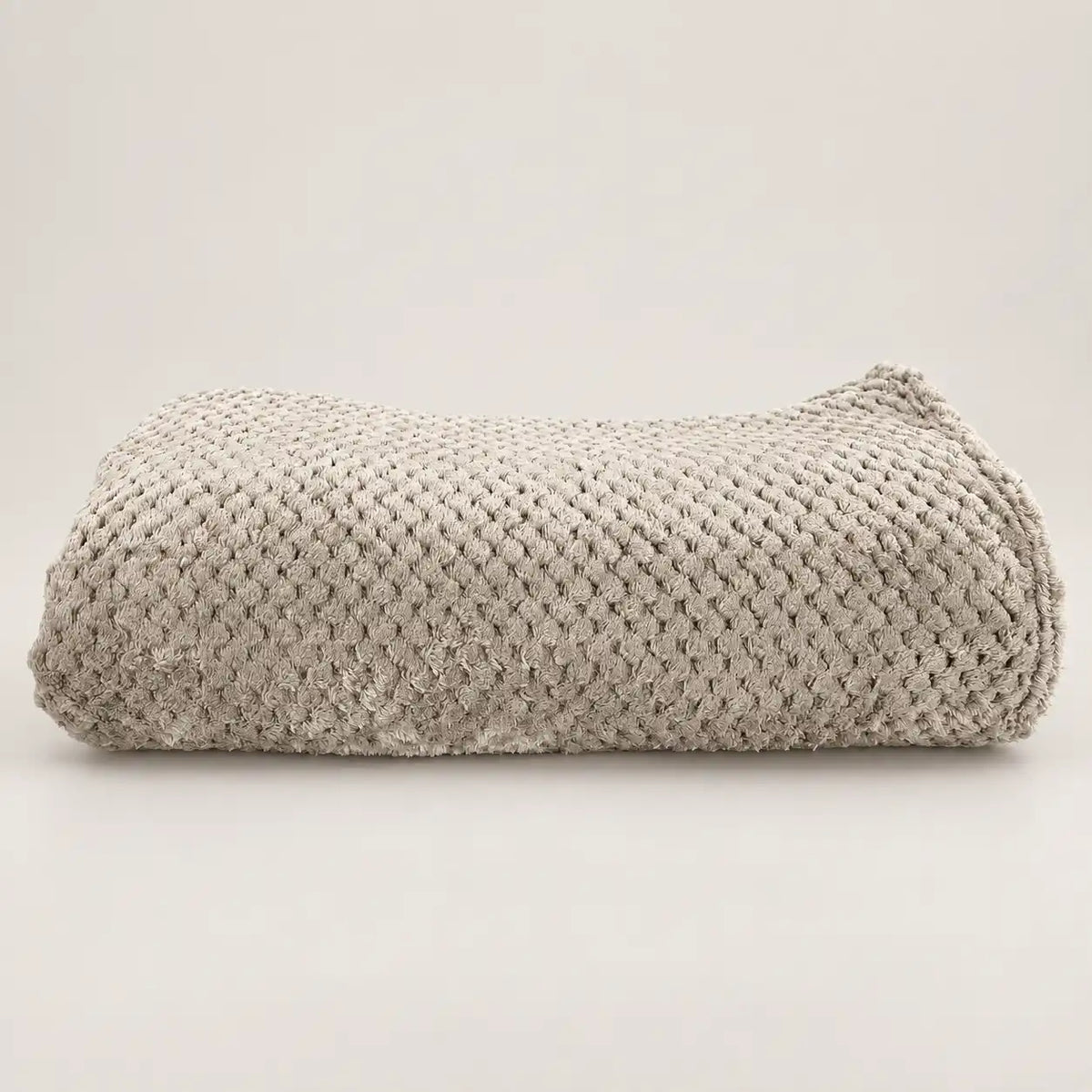 Manta polar fina y extra suave de color beige doblada sobre madera, mostrando su relieve texturizado.