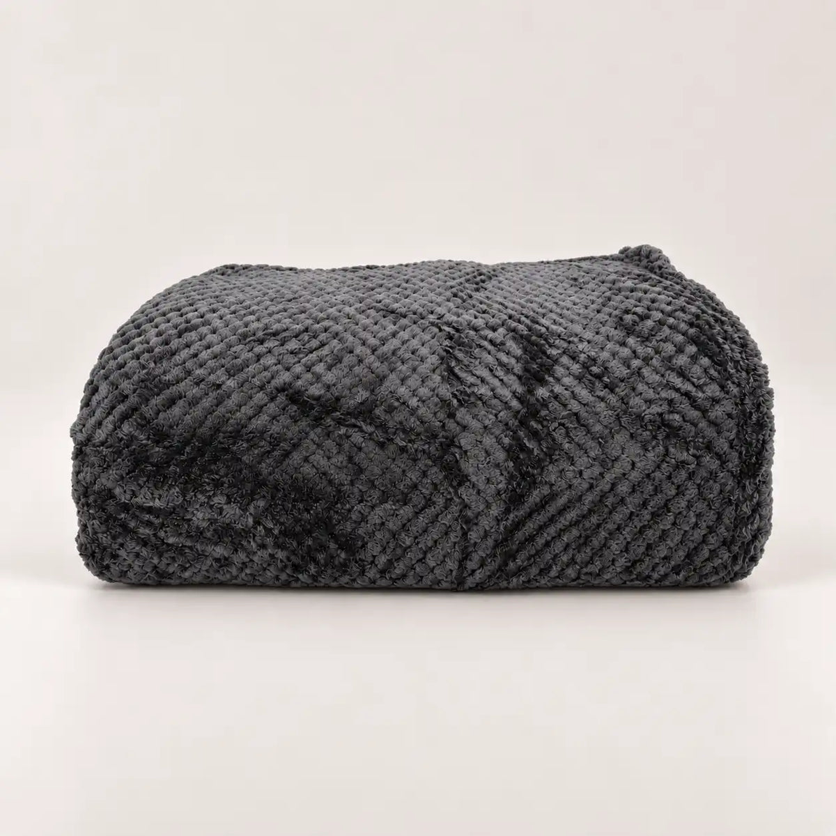 Manta polar fina y extra suave de color gris oscuro doblada sobre madera, mostrando su relieve texturizado.