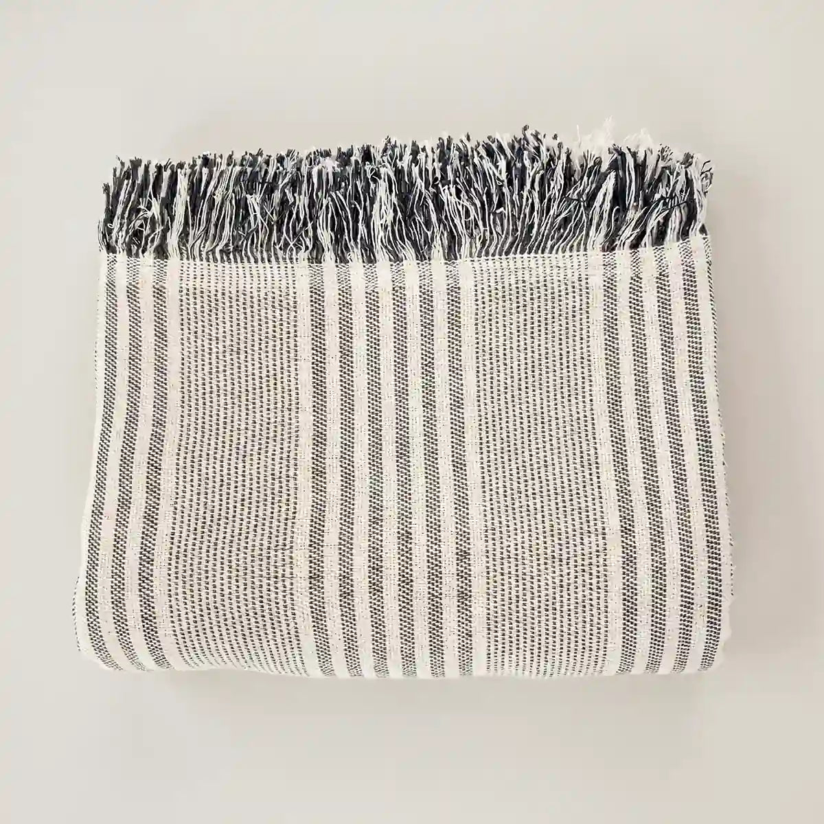 Plaid multiusos a rayas grises, ideal para guardar en cestas decorativas junto al sofá.